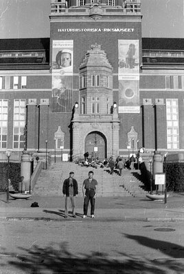 Exterior view of the Naturhistoriska Riksmuseet building. Two men stand in the foreground on a paved area, while other people...