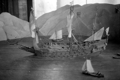 A black and white photograph of a detailed model sailing ship with multiple masts and sails. Two smaller model boats are posi...