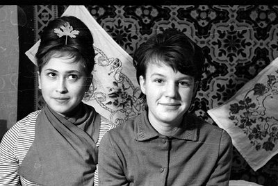 Black and white portrait of two young women sitting side-by-side. The woman on the left wears a striped shirt under a draped ...