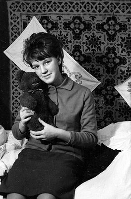 A black and white photograph of a person lying on a patterned rug and white pillows. The person is wearing a long-sleeved top...