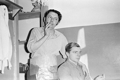A black and white photograph oriented upside down showing two people. One person is wearing a light-colored shirt and has the...