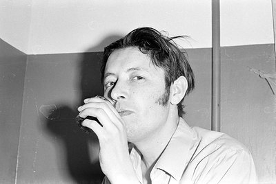 Black and white close-up of a man with sideburns holding a glass to his lips. He is wearing a light-colored collared shirt an...