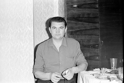 A black and white photograph of a man wearing a light-colored button-down shirt. He is positioned upside down in the frame, w...