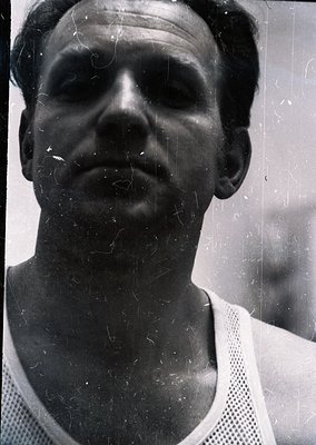 Vintage black-and-white portrait of a man in a mesh athletic jersey, likely from the 1960s–1970s. Close-up shot with visible ...