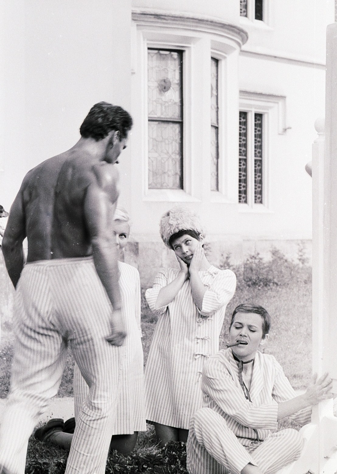 Two women and a man in striped costume on the grass in front of a pale stone façade