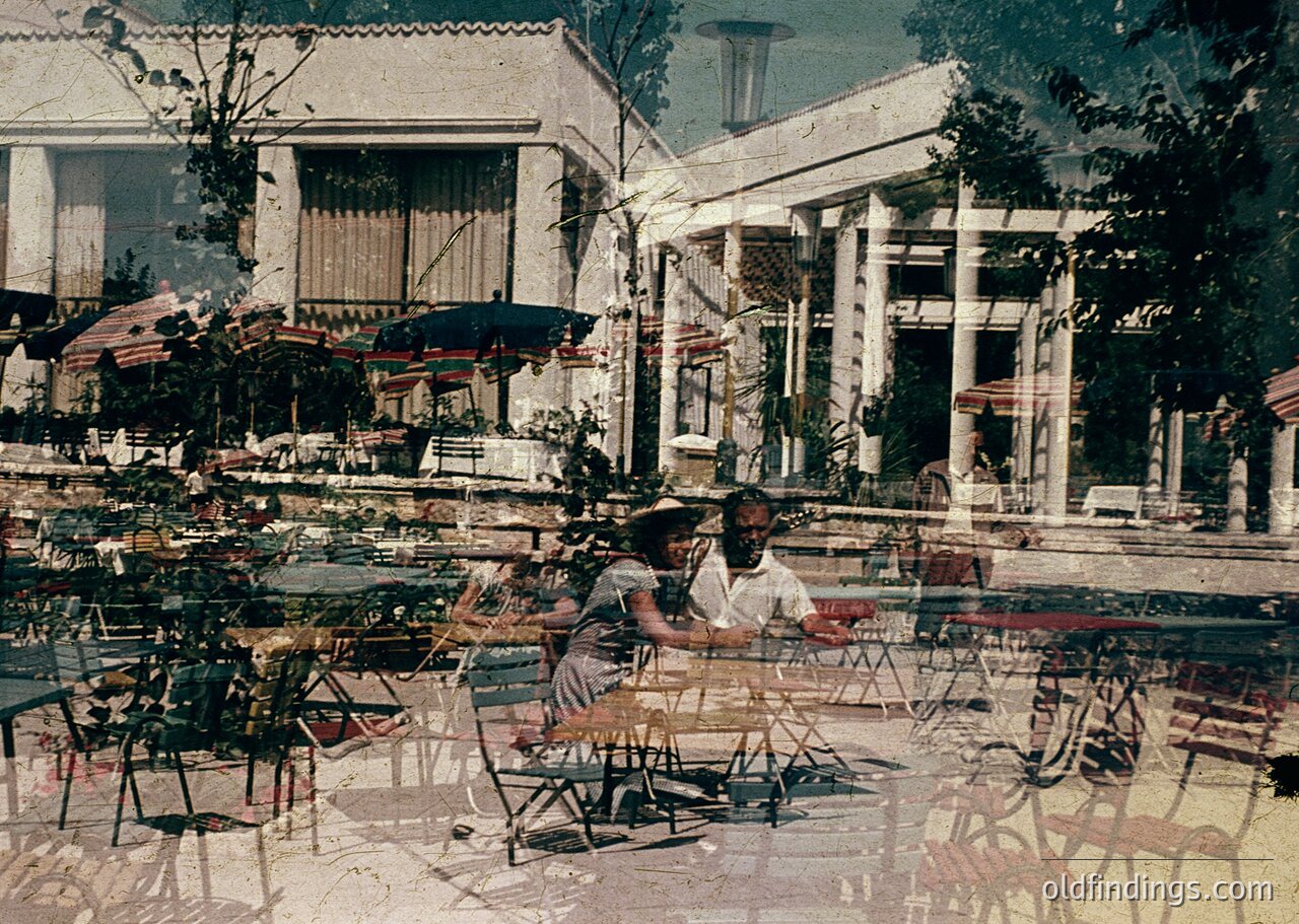 Vintage seaside café with neoclassical columns and tiled pool reflecting vintage seating. Two women in 1960s swimwear relax at a table, surrounded by wicker chairs and tables. Lush greenery and palm trees frame the scene, suggesting a Mediterranean or coastal European setting. é
