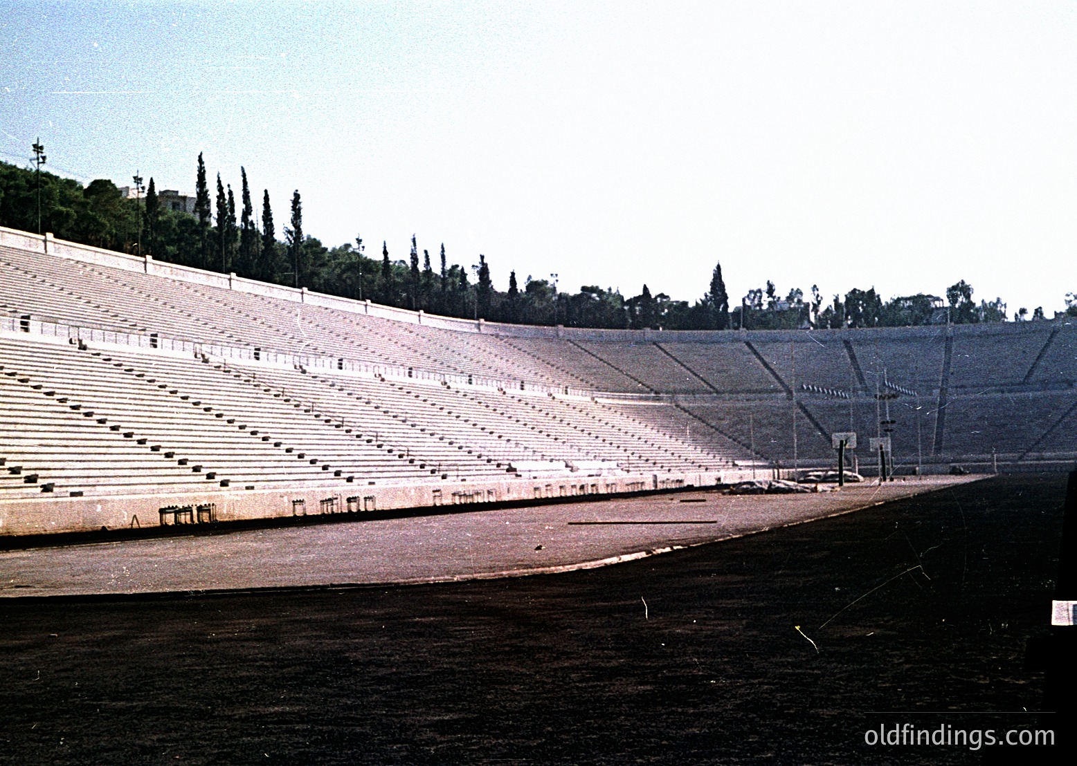 Panathenaic Stadium, Athens, Greece—iconic 19th-century marble stadium built for the 1896 Olympics, still in use. Symmetrical tiered seating with natural limestone, surrounded by pine trees. Empty track and field area under clear skies.