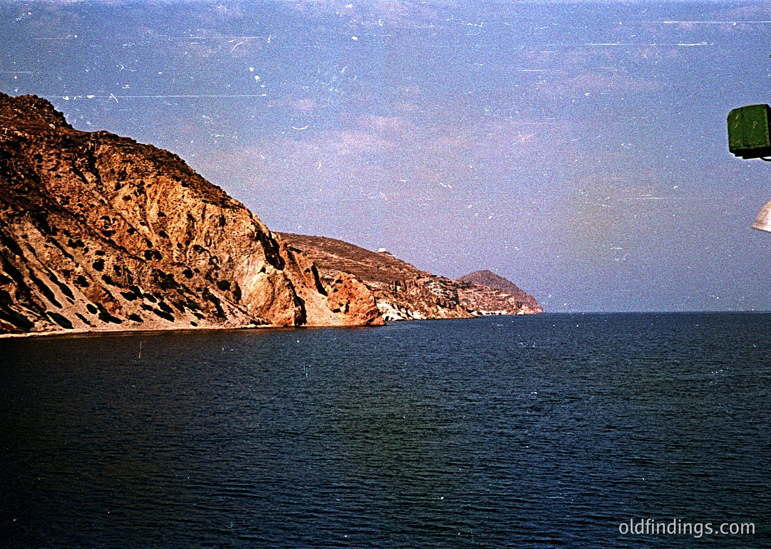 Vintage coastal scene featuring rugged, layered cliffs meeting deep blue waters. Partial view of a green lifebuoy on right suggests maritime setting. Likely Mediterranean or Black Sea region, mid-20th century.