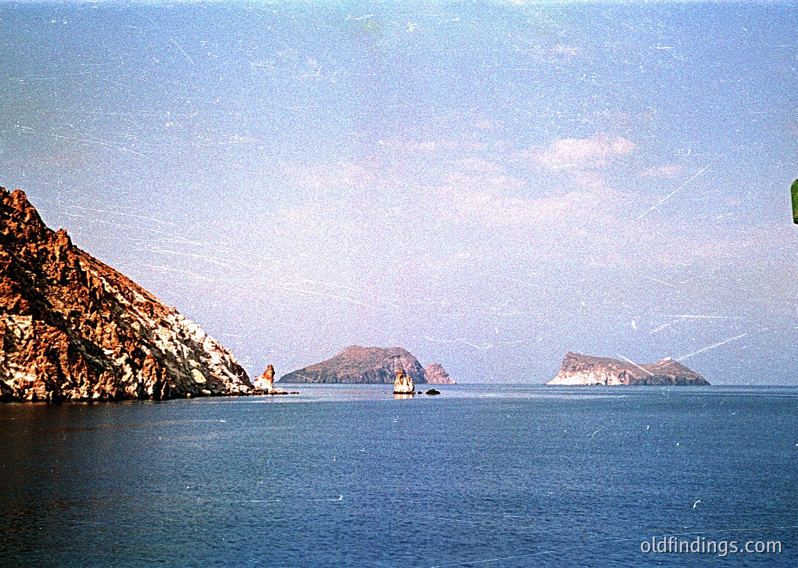 Vintage coastal scene featuring jagged limestone cliffs and two small rocky islets in calm waters. Soft vintage filter suggests 1970s–1980s photography. Ideal for historical or travel reference.