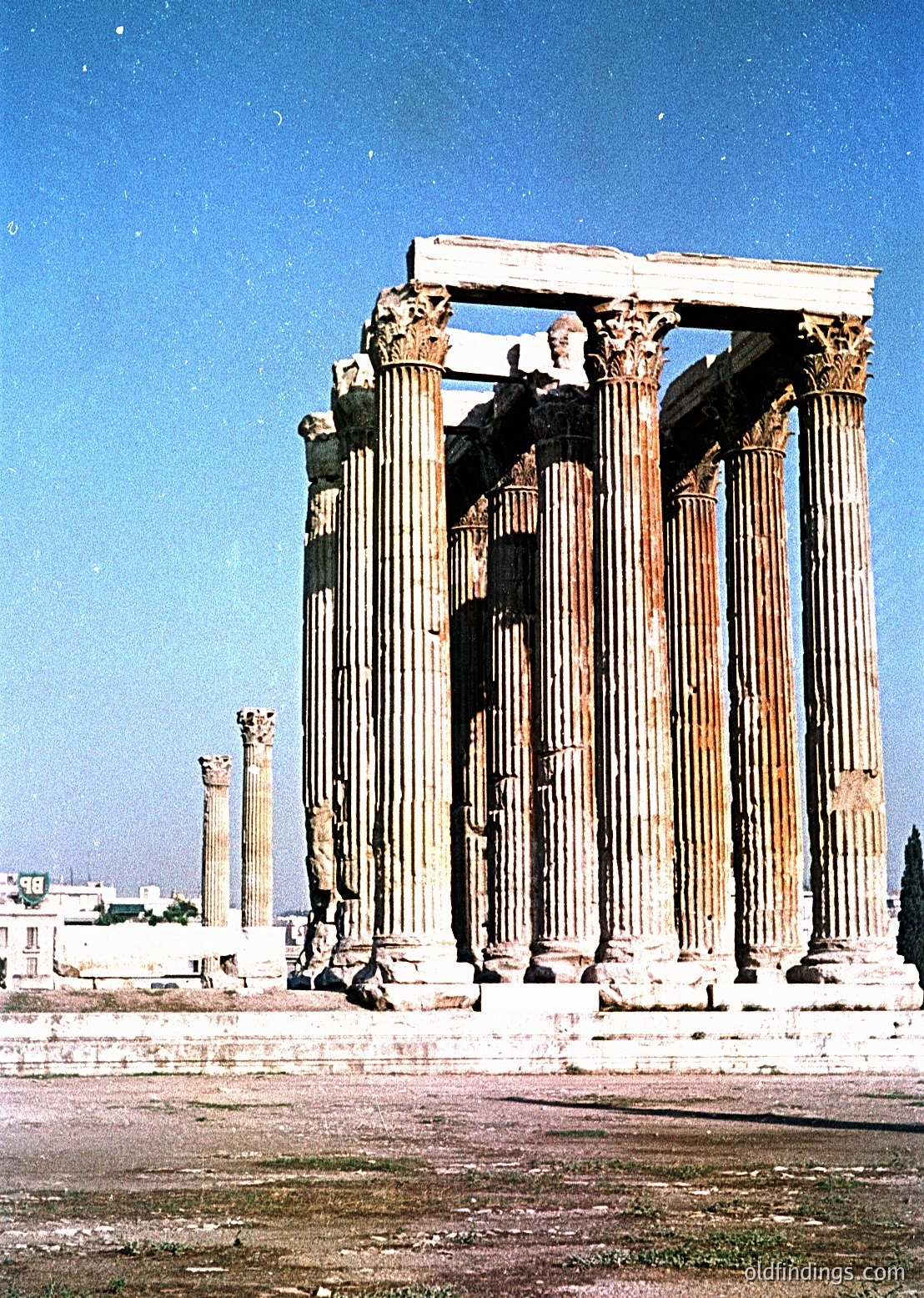 Ancient Greek-style ruins featuring **Doric columns** with weathered capitals, likely part of the **Temple of Artemis** in Ephesus, Turkey. Constructed from limestone, the columns exhibit classical fluting and minimal ornamentation. Urban backdrop suggests modern cityscape nearby.
