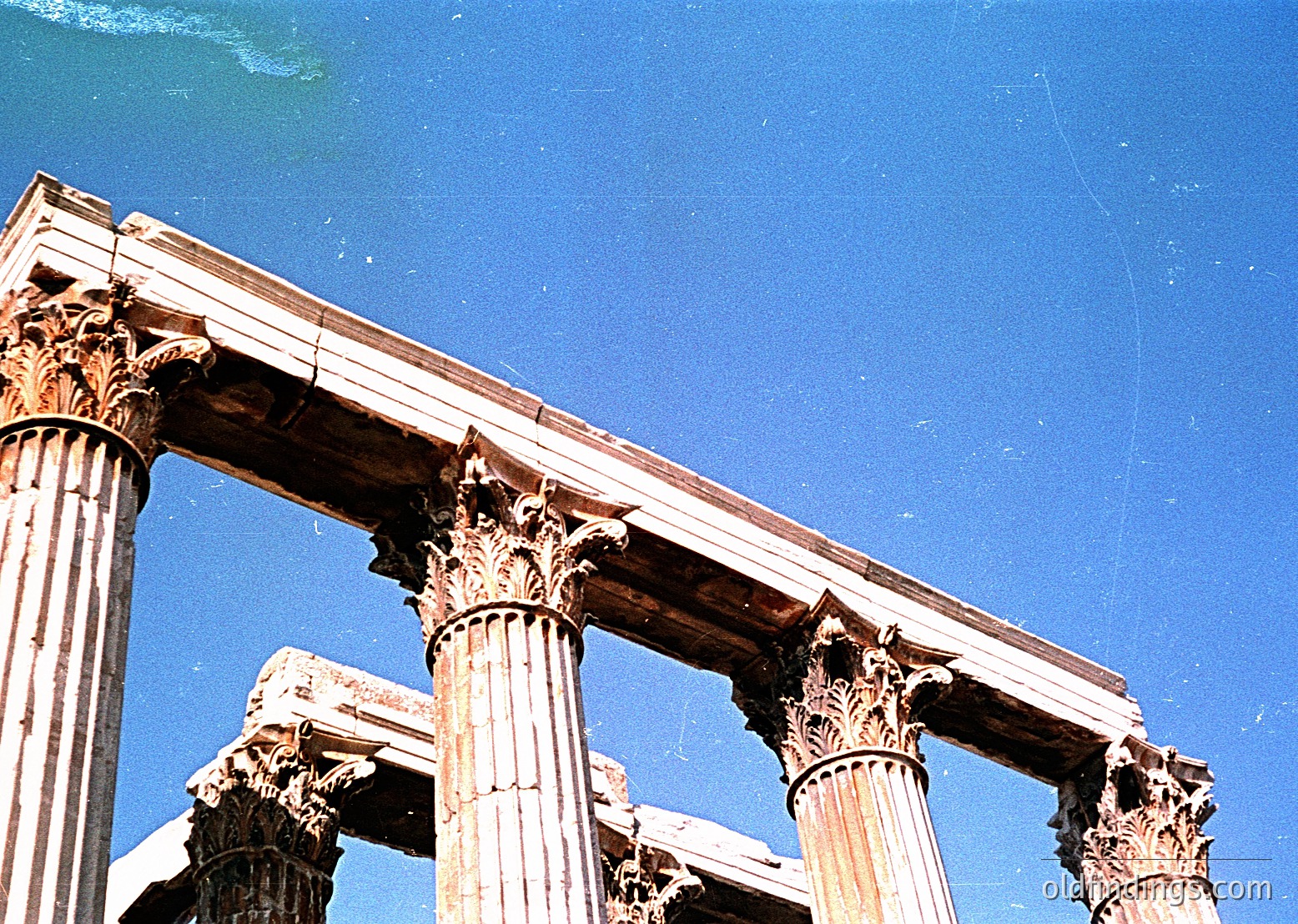 Ancient Corinthian columns with ornate capitals under a clear blue sky, likely part of a Roman-era ruin. The weathered stonework suggests classical architecture from the 1st–3rd century CE. Potential site: **Baelo Claudia (Spain)** or similar Mediterranean ruins.