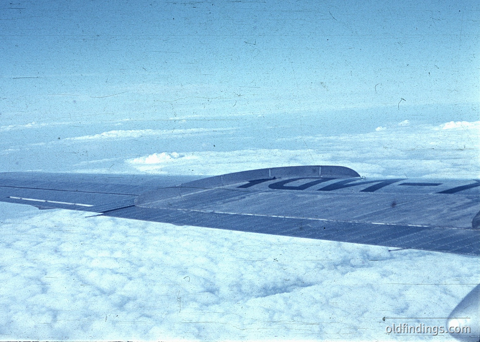 Aerial view of a snow-covered, flat landscape with a faintly visible road or path winding through the terrain. The sky is clear with scattered clouds, and the image appears aged with a vintage tint. [Mid-20th century aerial photography of snow-covered terrain with faint road markings, likely for agricultural or surveying purposes ]