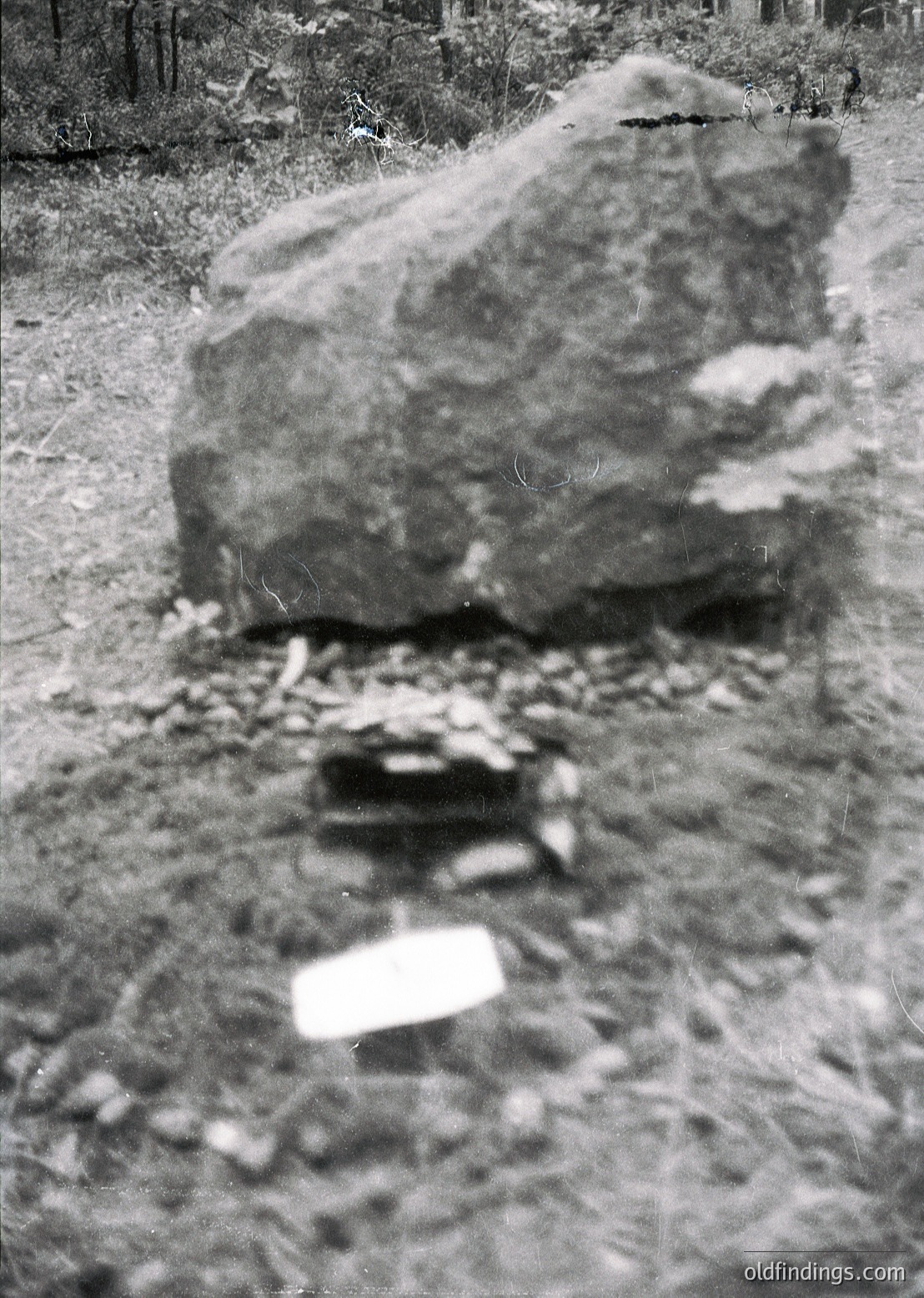 Blurred vintage monochrome shot of a large, irregularly shaped boulder on a gravel path, surrounded by scattered stones and foliage. Likely mid-20th century outdoor scene, possibly a park or forest trail.