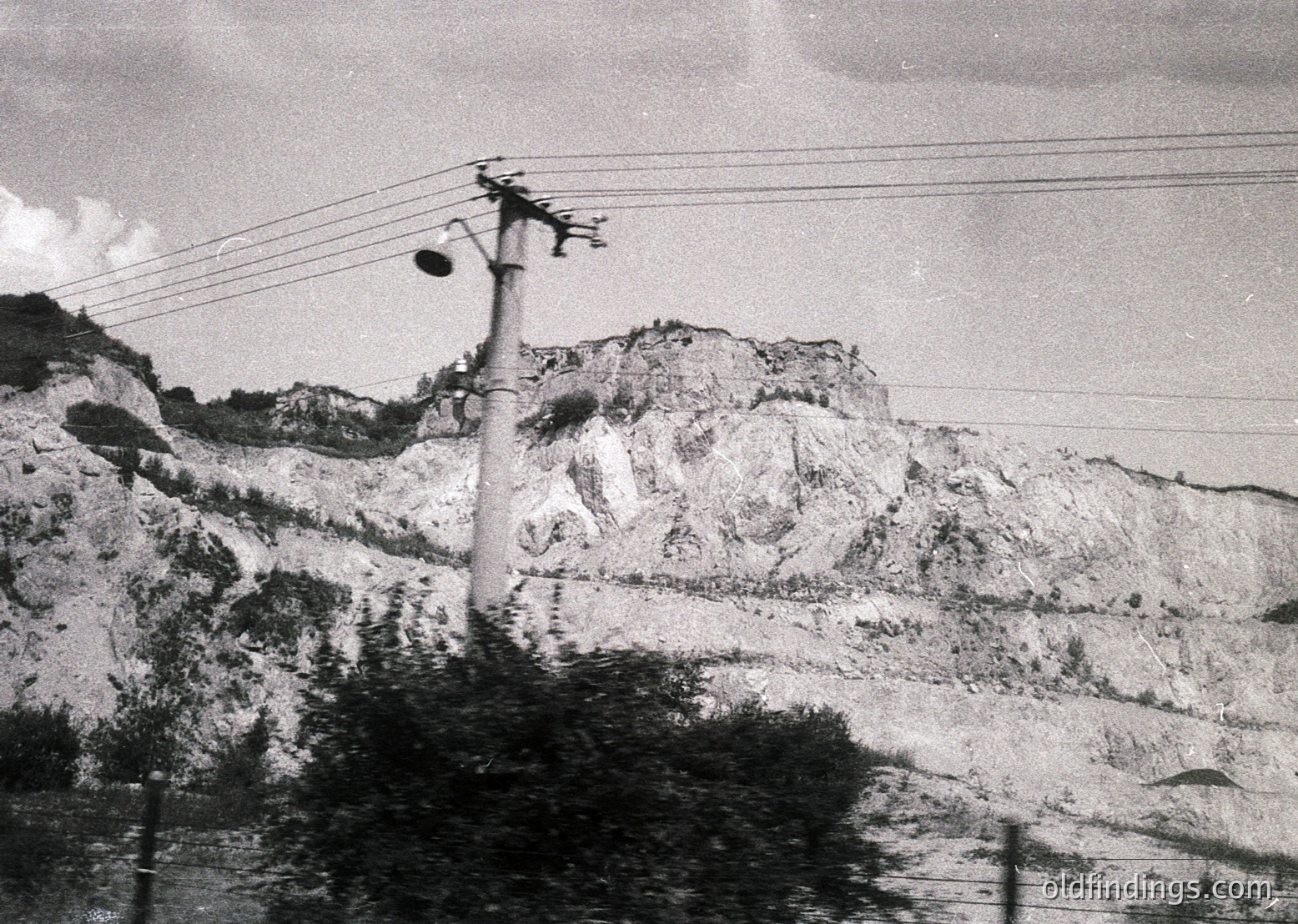 Mid-20th century black-and-white photo of rugged mountainous terrain with utility pole and power lines. Barren hillsides suggest early industrialization or post-war landscape.