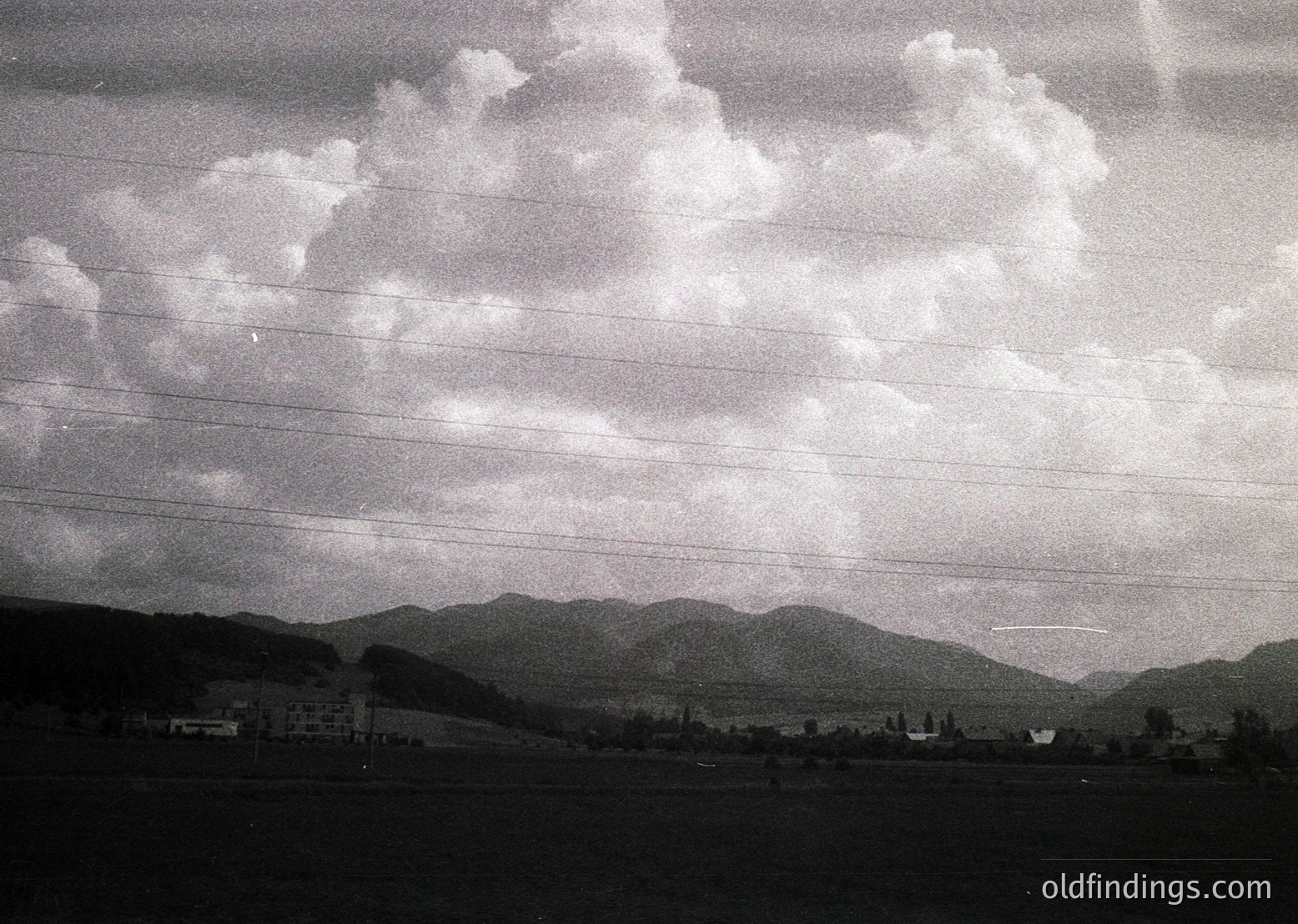 Black-and-white aerial view of rolling hills and scattered buildings, framed by horizontal window bars. Likely mid-20th century architecture with industrial or institutional design. Landscape suggests rural or suburban setting.