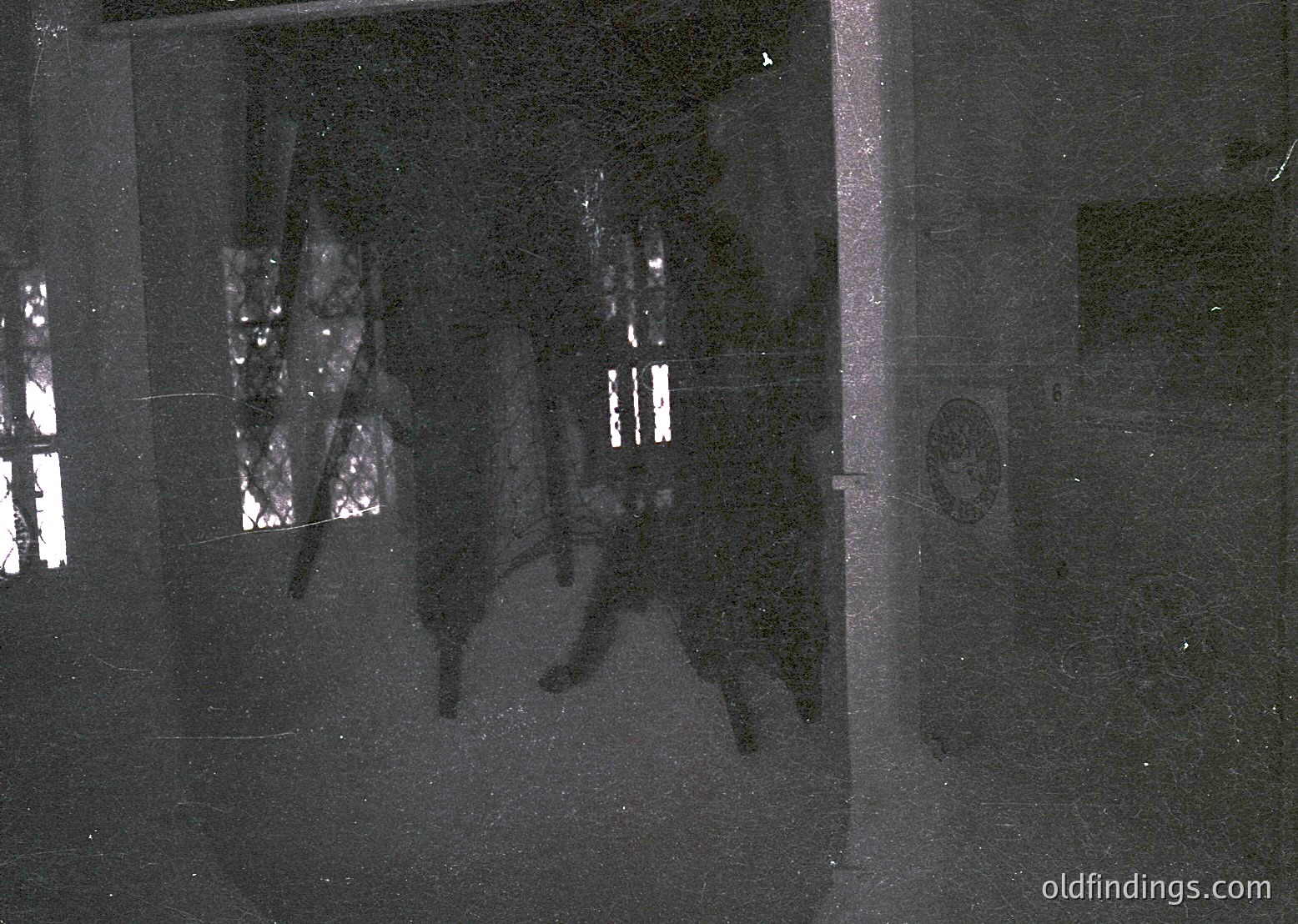 Vintage grayscale shadow projection on a textured wall, likely from a slide projector. Silhouettes of two figures in mid-stride, one carrying a rectangular object. Reflective surface suggests an indoor setting, possibly a 1960s–1980s home or classroom. *(Note: Due to low detail, specifics like location or exact time period remain speculative.)*