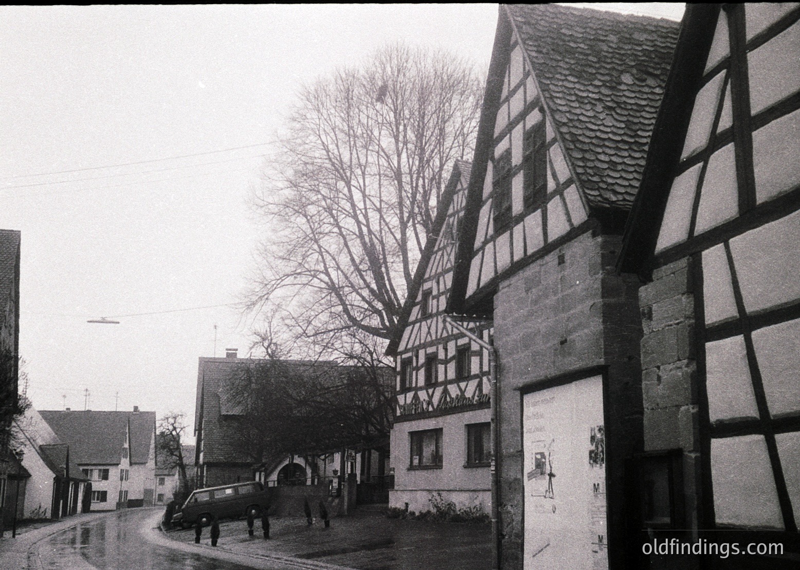 Classic timber-framed half-timbered houses dominate this mid-20th century European village street. The steep-pitched roofs and exposed wooden beams reflect traditional , likely . A vintage car and pedestrians add to the nostalgic atmosphere. Ideal for historical research or vintage design inspiration.