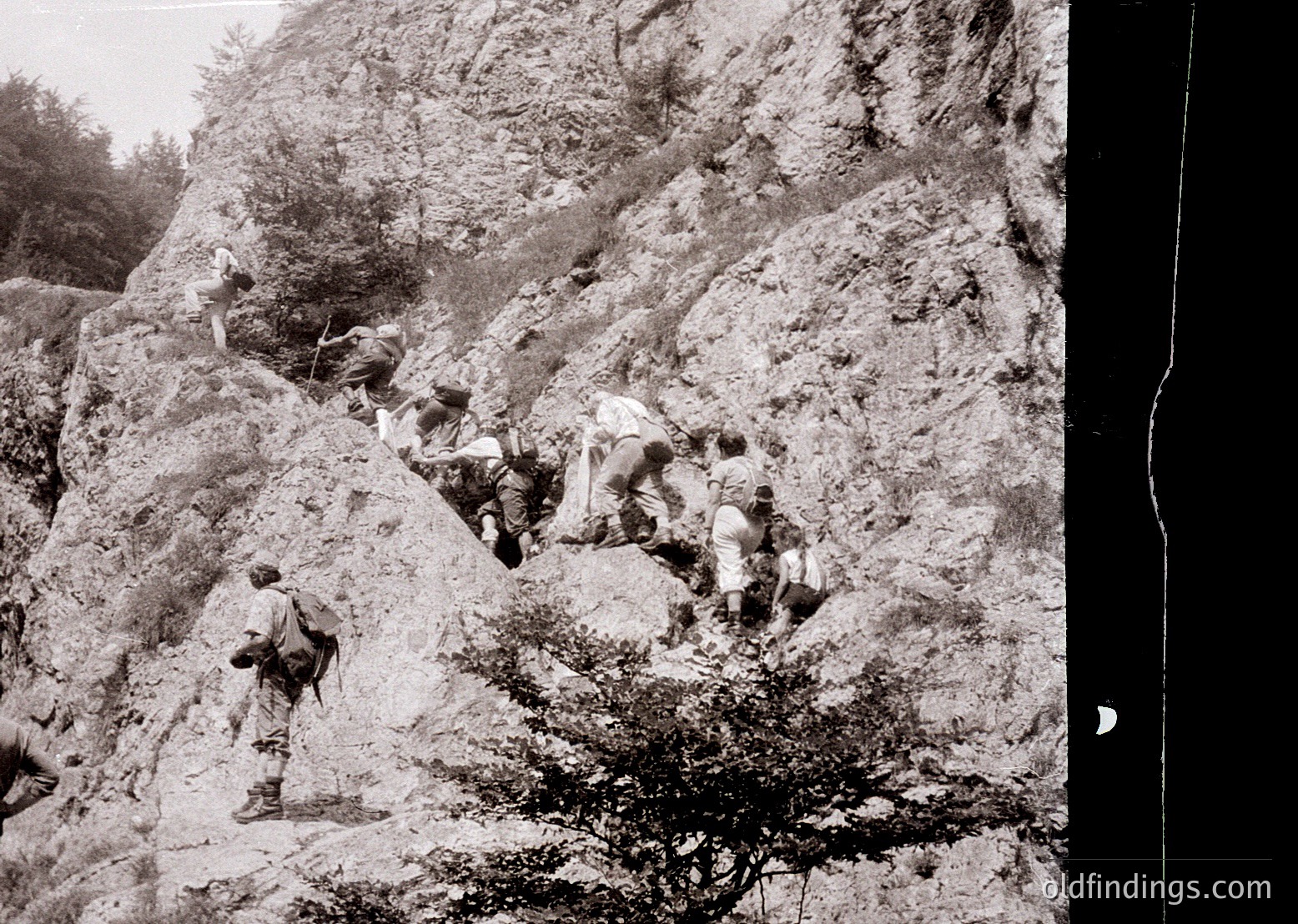 Black-and-white photo of a group of soldiers ascending a rugged, rocky mountain trail, likely during WWI or WWII. Uniforms suggest military training or combat conditions.