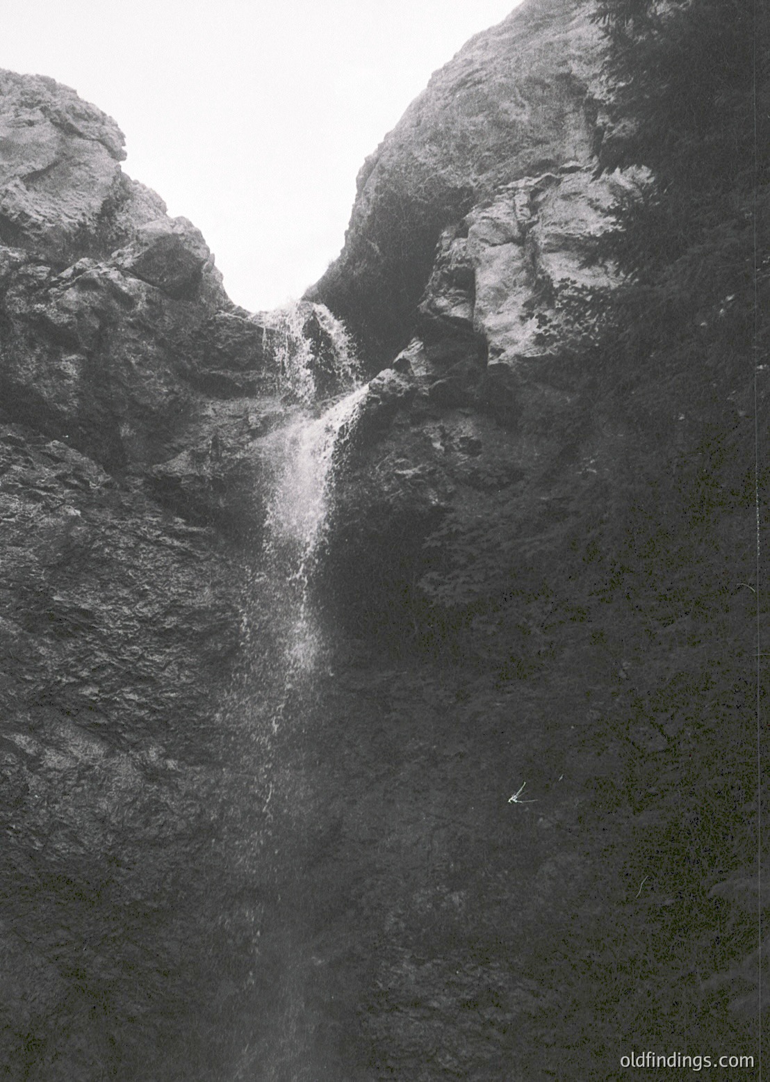 Powerful waterfall cascading between rugged rock walls, framed by dense forest. Dramatic vertical composition highlights mist and raw natural texture. Ideal for nature, adventure, and landscape photography.