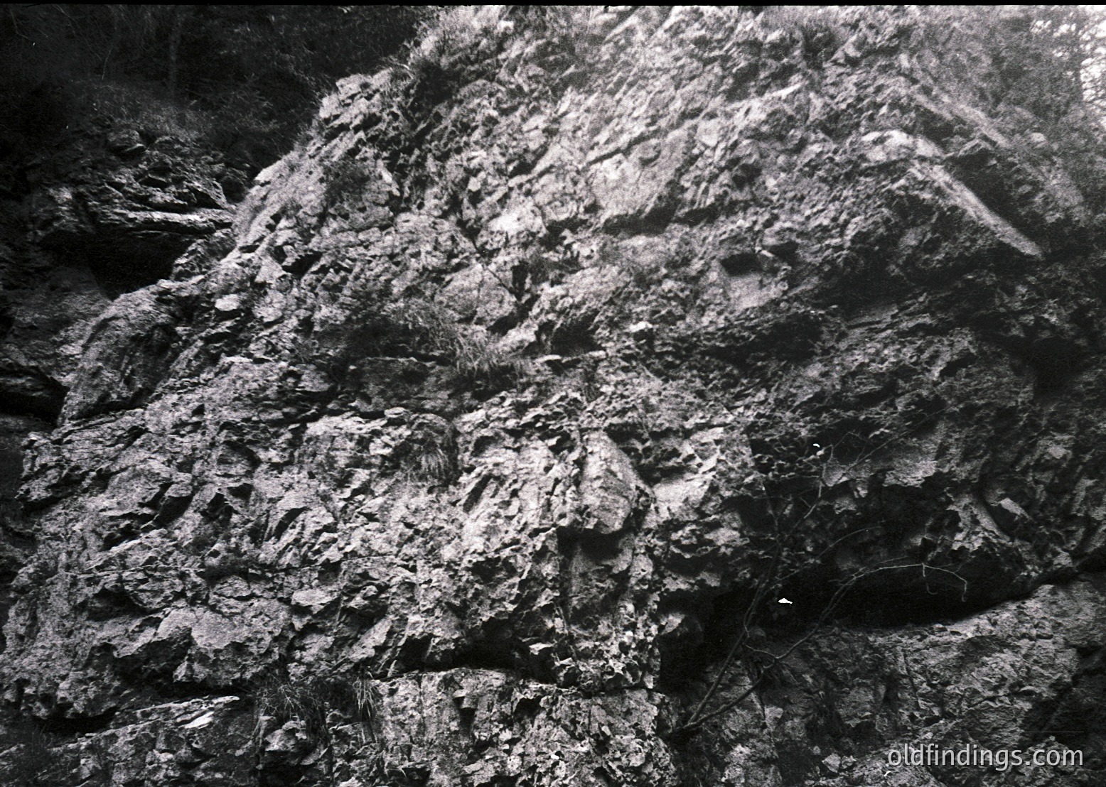 High-contrast black-and-white close-up of rugged, layered rock formations resembling human facial contours. Texture suggests sedimentary erosion, likely in a cave or cliffside. Style evokes mid-20th century documentary photography.