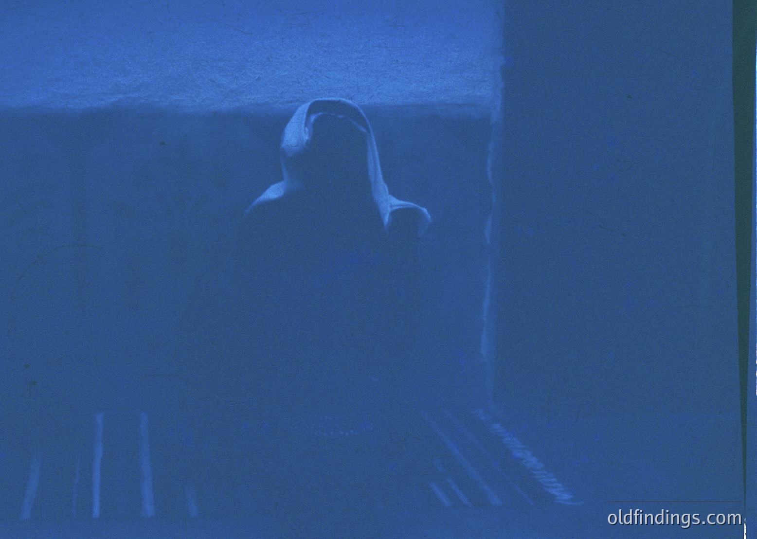 Silhouette of a person standing in a dimly lit interior, back to camera, with blurred vertical lines (likely curtains) framing the scene. Moody, atmospheric lighting suggests evening or indoor photography. Potential use for mood-driven editorial or artistic projects.