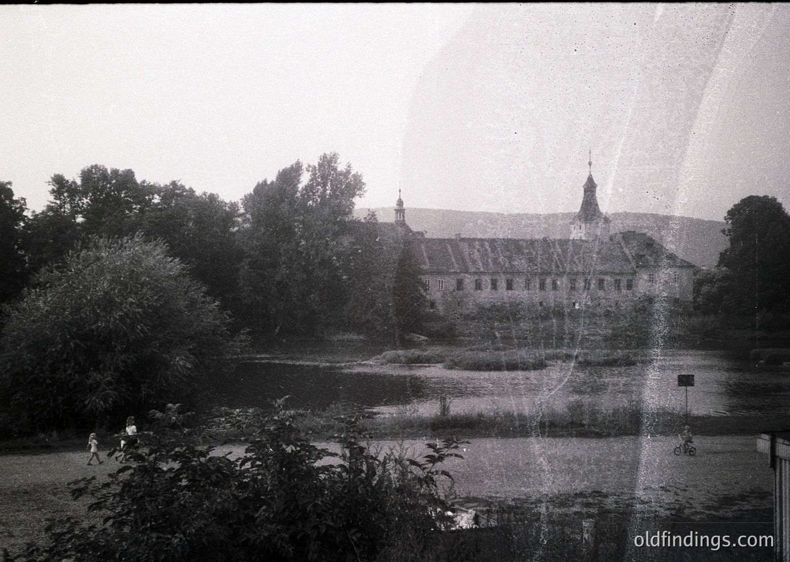 Historic castle-like building with symmetrical architecture, surrounded by dense greenery and a pond. Likely Eastern European *(Note: The image lacks clear identifiers for precise location, but the style suggests a European castle or palace from the 19th century.)*