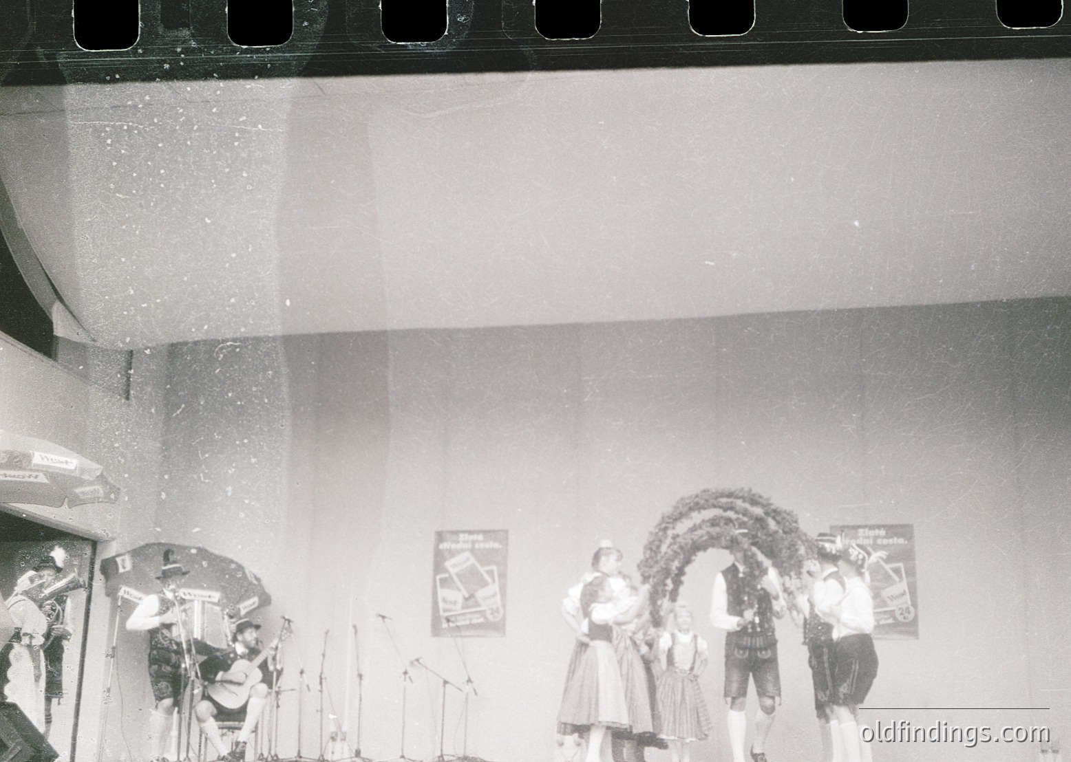 Mid-century stage performance with fog machine creating atmospheric haze. Stage setup includes microphones, a decorated archway, and a banner reading "Bayerische Volksfest." Traditional Bavarian attire visible among performers. Likely a folk or cultural festival event, 1950s–1970s.
