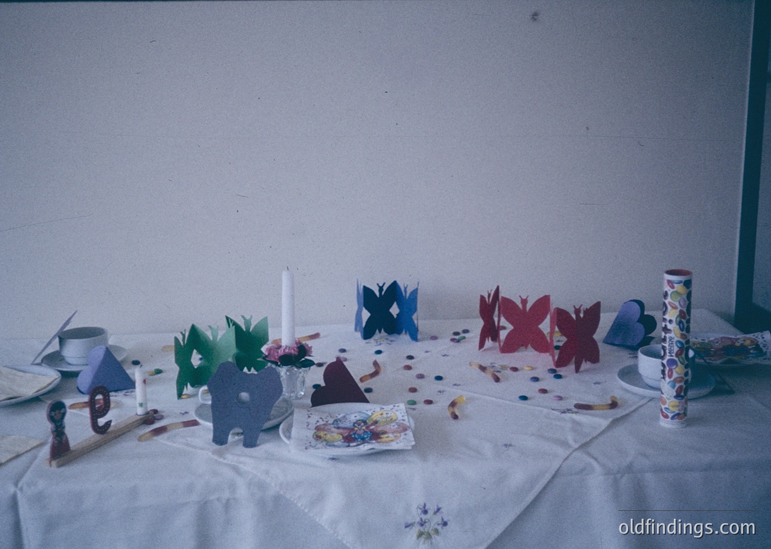 Handcrafted paper butterflies, elephants, and geometric shapes decorate a tabletop with confetti and a lace tablecloth. Mid-20th century craft project or classroom activity, likely or . Potential use for vintage education, DIY inspiration, or historical craft research.