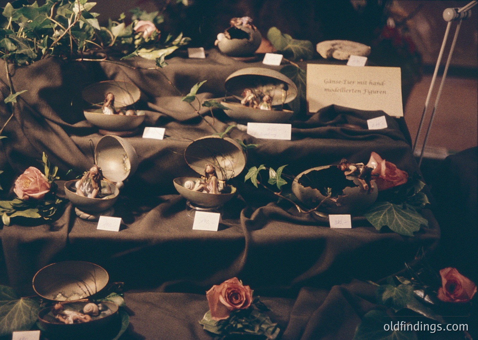 Vintage ceramic goose figurines with hand-modeled features displayed on a draped table, surrounded by artificial foliage and roses. Likely from a 1960s–1970s German craft exhibition or home decor collection.