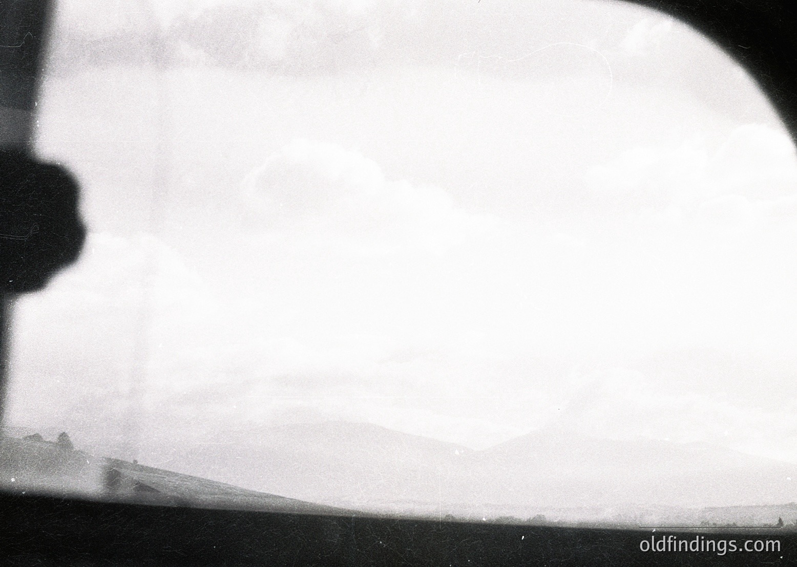 Vintage aerial view through a curved aircraft window, showing hazy terrain below. Distinctive low-lying clouds obscure details, suggesting early aviation photography. Likely mid-20th century due to film grain and framing.