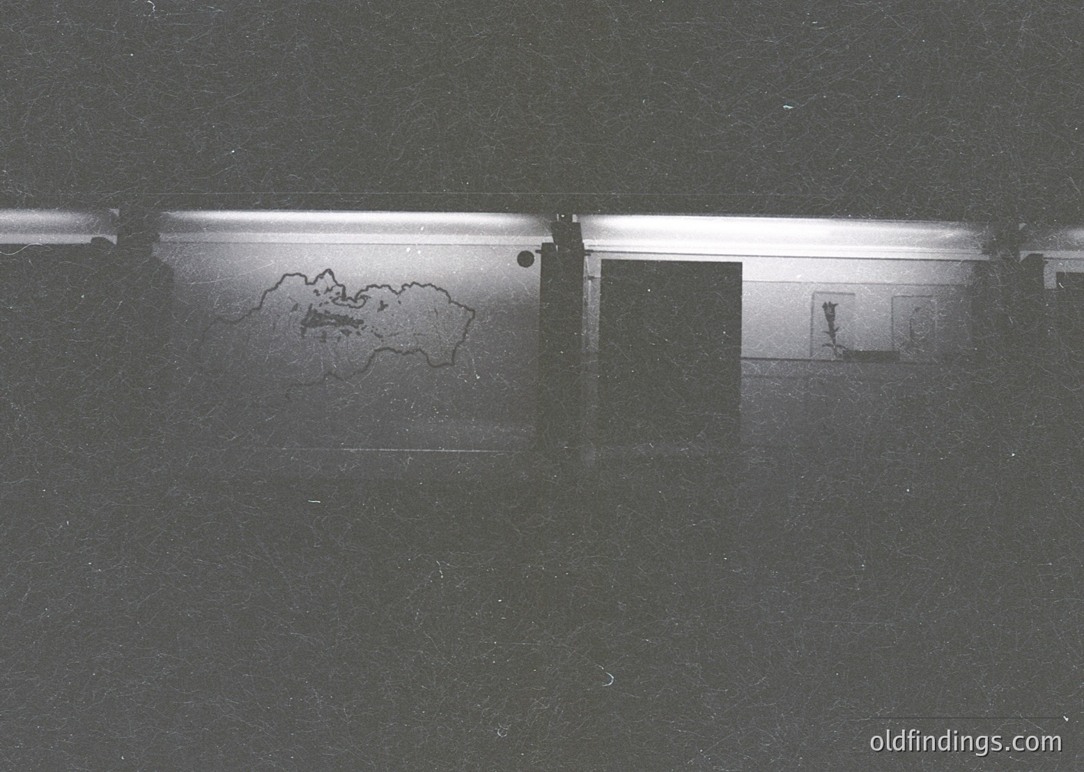 Black-and-white photo of a flooded hallway with a map outline of Bulgaria etched into the wet wall. Minimalist interior features a single door and fluorescent lighting. Likely 1970s–1990s Eastern Bloc architecture.