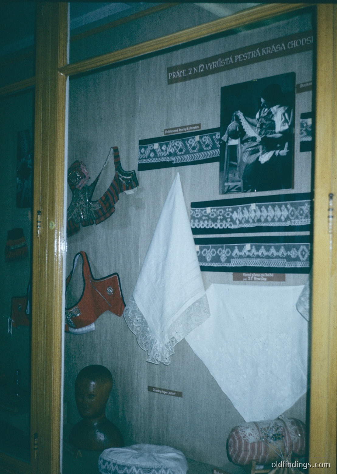 Vintage folk costume display featuring embroidered textiles, traditional footwear, and headwear. Text in Czech suggests cultural heritage exhibit (, , , , ).