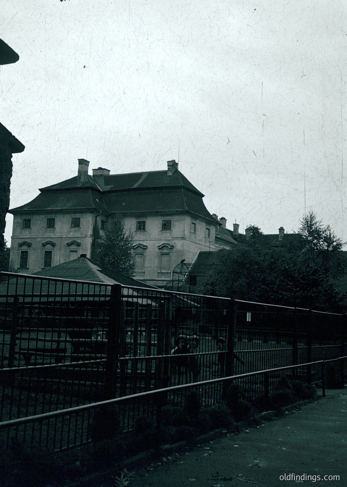 Neoclassical building with symmetrical façade, arched windows, and slate roof behind wrought-iron fence. Likely institutional or governmental architecture from mid-20th century.