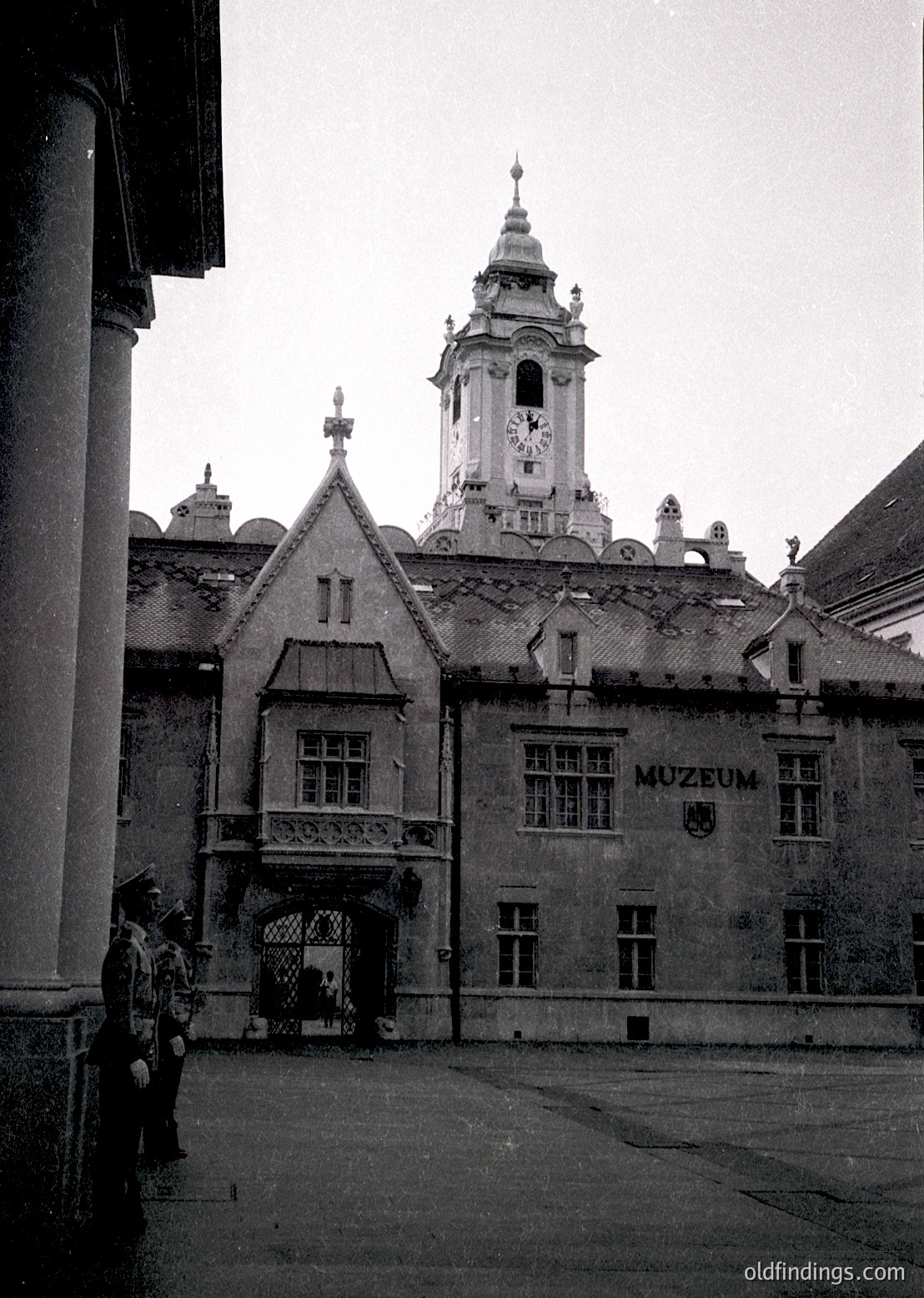 Historic courtyard entrance to a museum building with Gothic Revival architecture—steeple clock tower, arched gateway, and stone façade. Signage reads "MUZEUM" in Cyrillic. Likely Eastern European, mid-20th century.