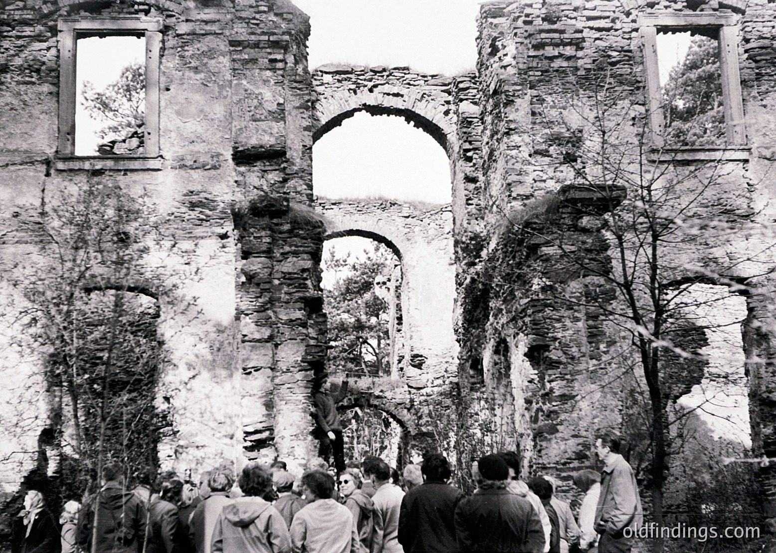 Ruins of a historic stone church with arched windows and crumbling walls, surrounded by a crowd of people. Architectural details include large arched doorways and remnants of decorative stonework. Likely Eastern European, mid-20th century.