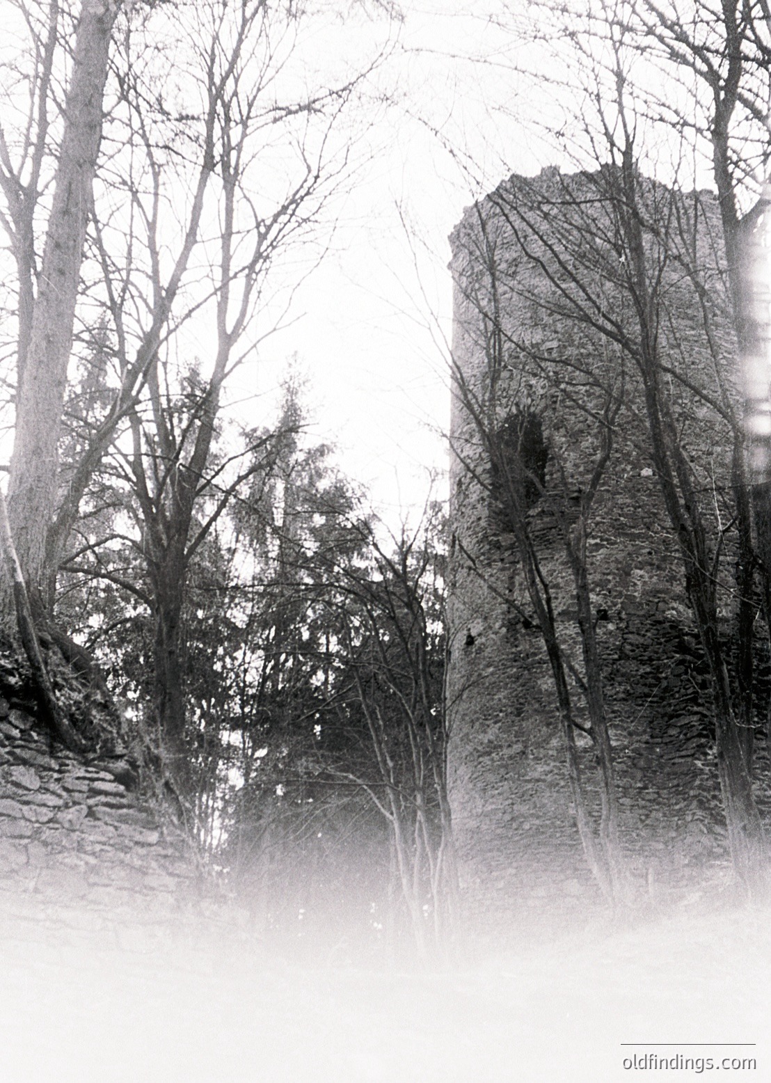 Vintage sepia-toned photograph of a mist-shrouded stone tower flanked by leafless trees, suggesting winter or early spring. The tower’s weathered texture hints at historical significance, possibly medieval or early modern. Fog obscures details, adding an atmospheric, timeless quality.