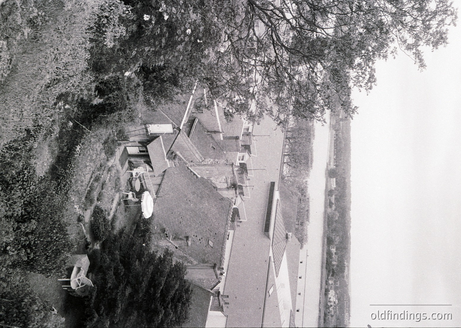 Aerial view of a coastal village with modest wooden structures and a narrow road. Dense greenery frames the scene, suggesting a seaside or lakeside setting. Likely mid-20th century based on architectural style and photographic grain.