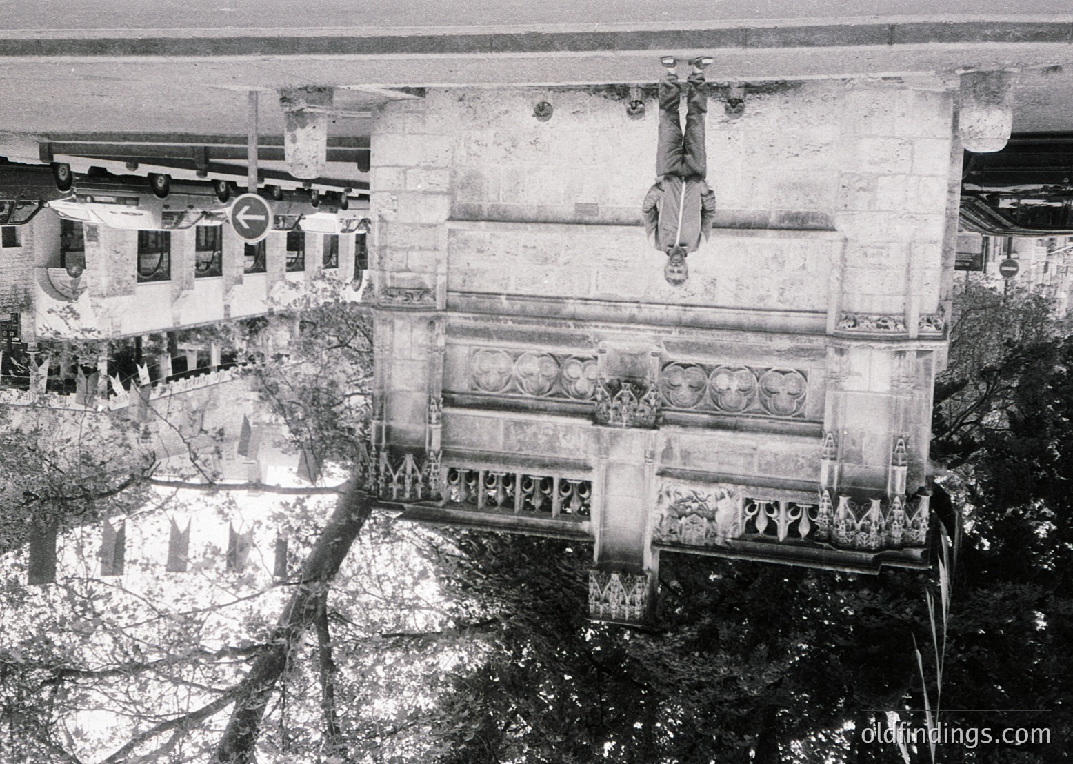 Aerial view of a grand, decaying neoclassical building façade with ornate balustrades and sculptural reliefs, likely from the early-to-mid 20th century. Surrounding greenery and adjacent structures suggest an urban park or historic district setting.