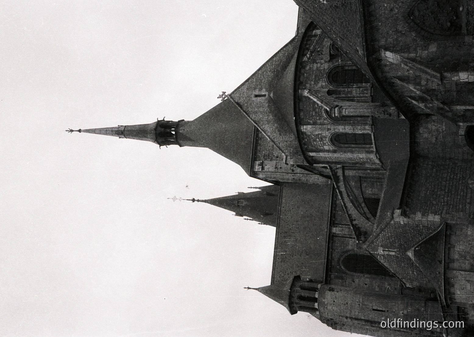 Aerial black-and-white photograph of a medieval fortress with steep, conical towers and crenellated walls, likely from the 12th–15th century. Architectural details include narrow slit windows and a central keep.