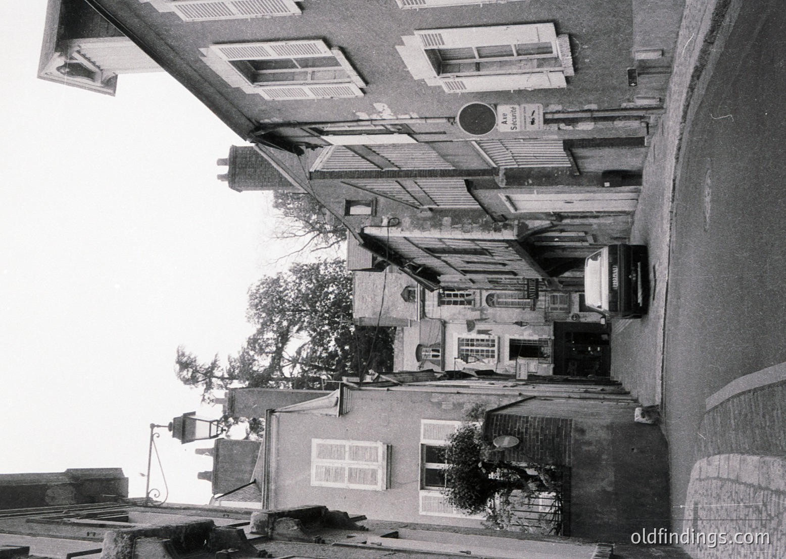 Urban courtyard framed by mid-20th century Soviet-era apartment blocks, featuring flat roofs, shuttered windows, and a central tree. Concrete staircases and utility pipes dominate the scene, reflecting post-war functionalist architecture.