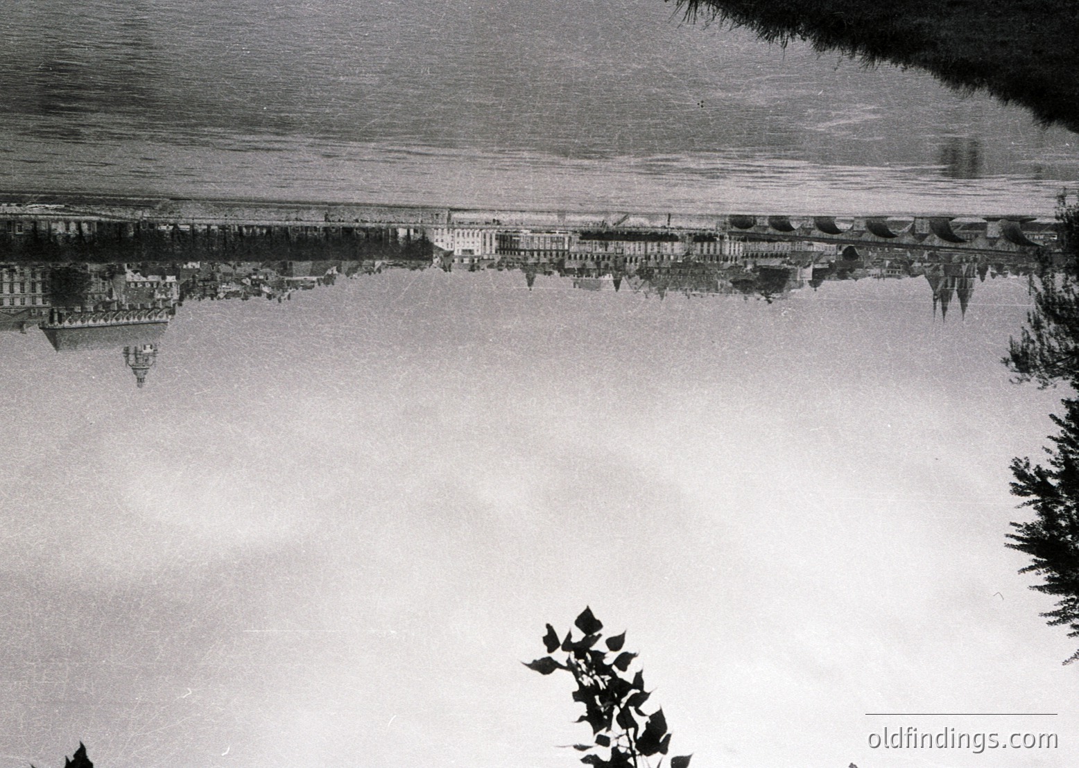 Symmetrical reflection of a grand, multi-story neoclassical building in a calm body of water, likely a lake or canal. Architectural details include columns, arched windows, and a central entrance. Blurred motion suggests long-exposure photography.