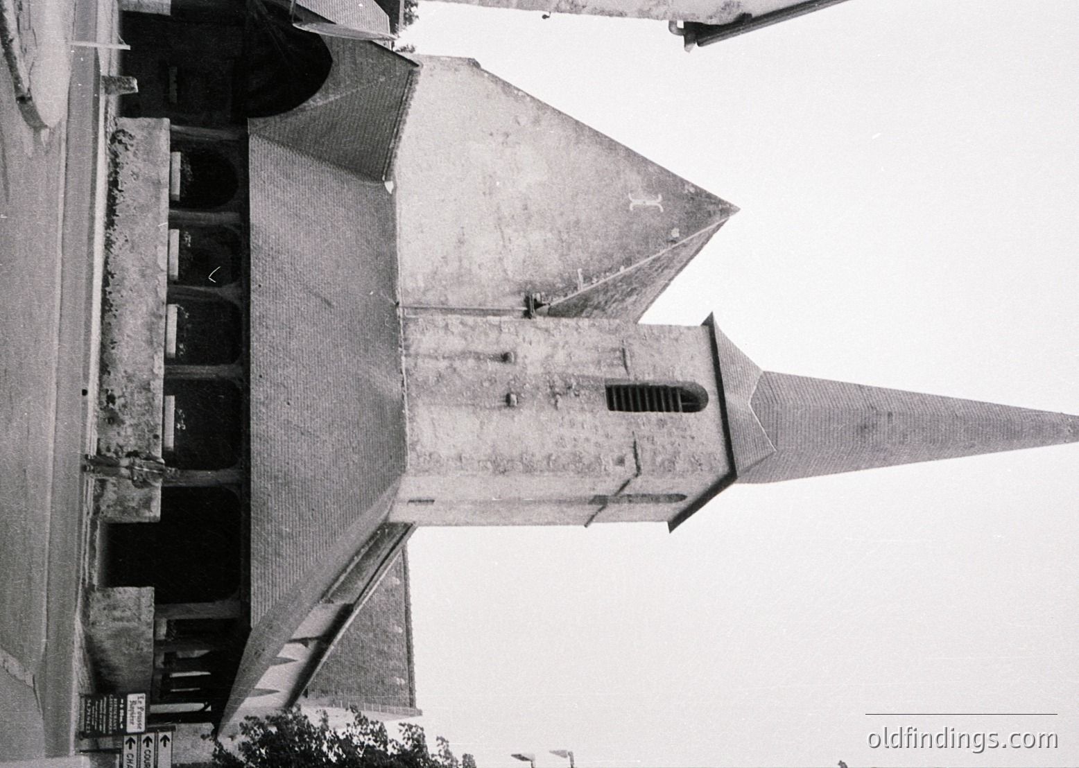 Aerial view of a Brutalist-style church steeple with exposed concrete and geometric detailing. The sharp, angular design features a tapered spire and vertical ventilation slits. Likely Eastern European, mid-20th century.