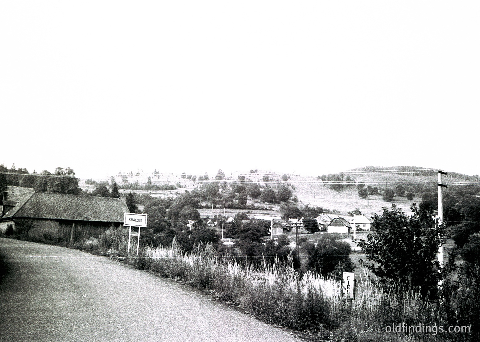 Rural village roadside scene with modest brick homes, overgrown vegetation, and a hand-painted "Varna" sign. Mid-20th century Eastern European countryside, likely Bulgaria.