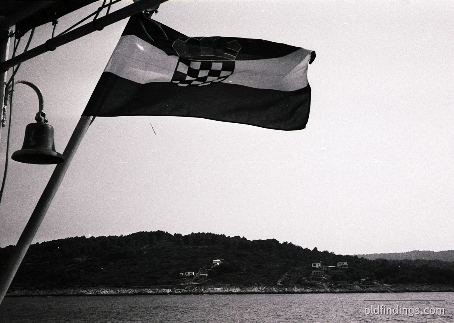 Croatian flag waves atop a ship’s mast beside a handbell, set against a calm coastal landscape. Black-and-white monochrome suggests mid-20th century.