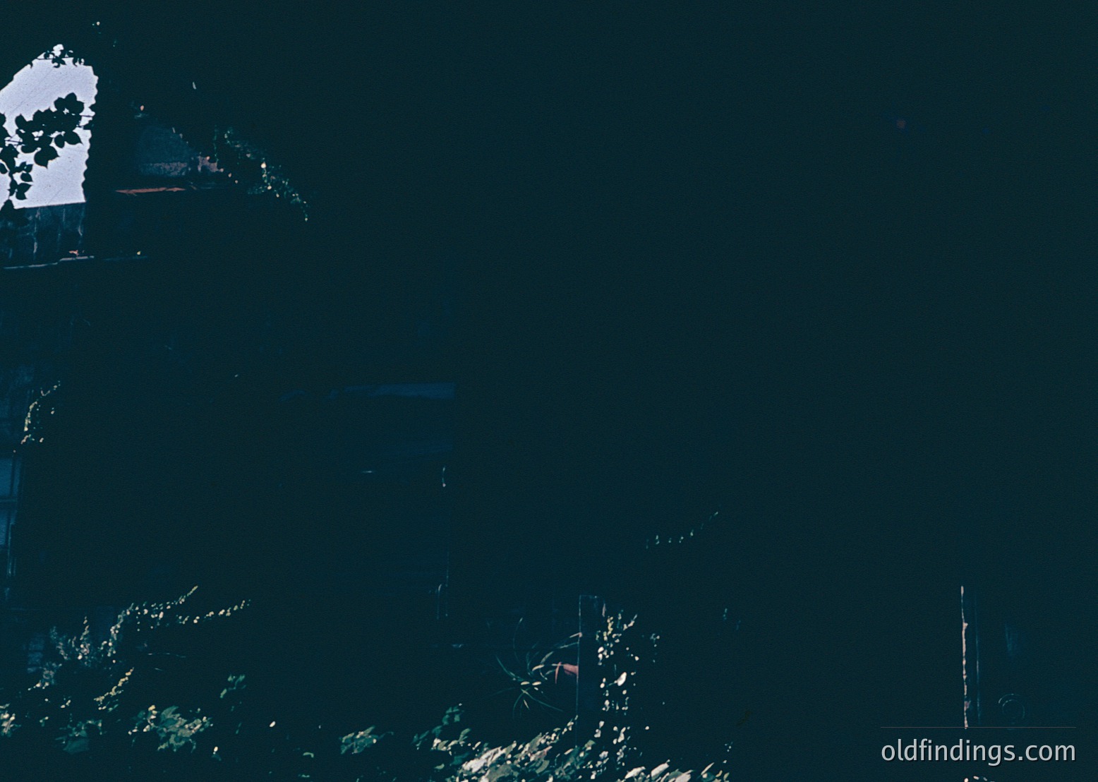 High-contrast aerial view of a coastal landscape with dark water and sparse vegetation. Distinctive white rock formation and faint shoreline visible. Likely a moody, atmospheric seascape with minimal human presence.
