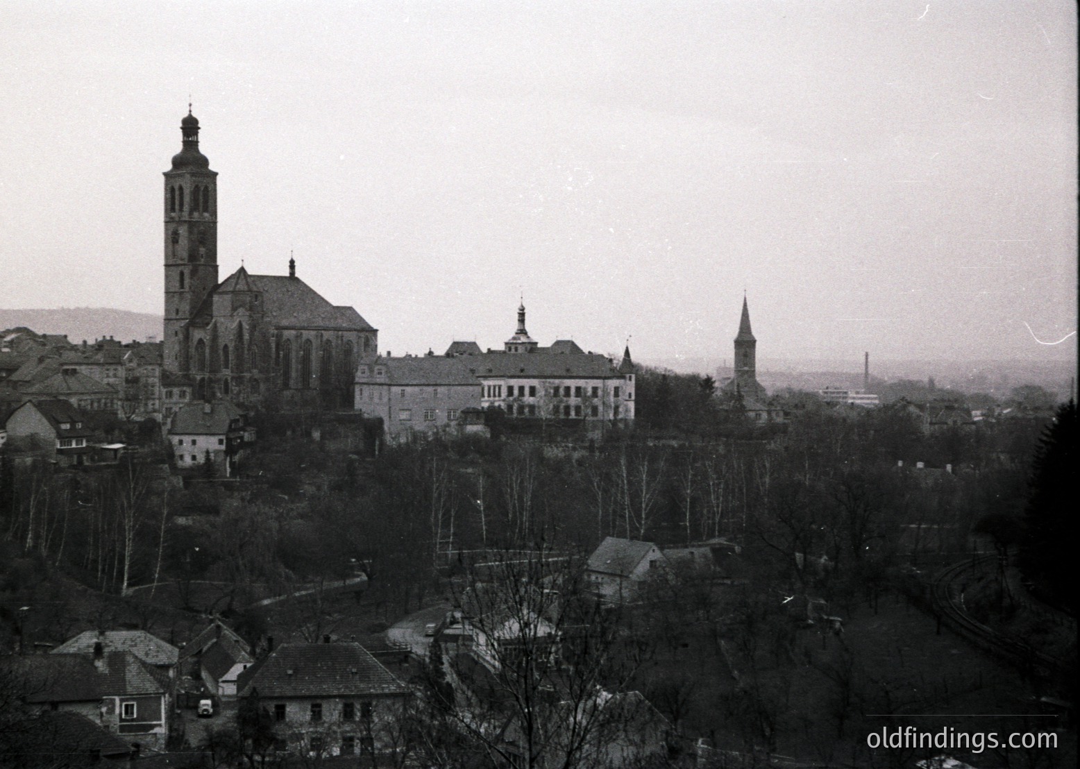 Black-and-white aerial view of a historic European town with a prominent church tower and cathedral spire. Dense rooftops and tree-lined streets suggest a pre-1950s urban layout. Industrial chimneys hint at early 20th-century development.