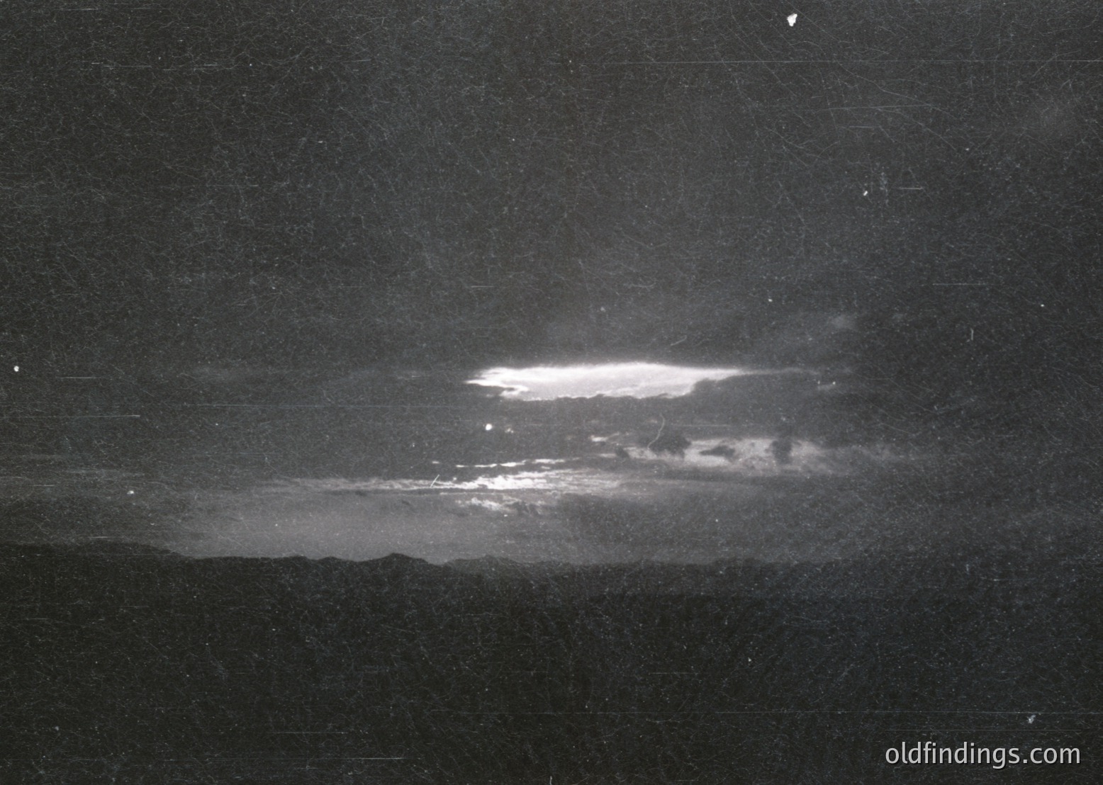Vintage high-contrast black-and-white photograph of a dramatic nighttime sky with a bright, elongated aurora borealis display. The celestial phenomenon dominates the upper center, casting an ethereal glow against the dark horizon. Likely captured with early 20th-century photographic techniques.