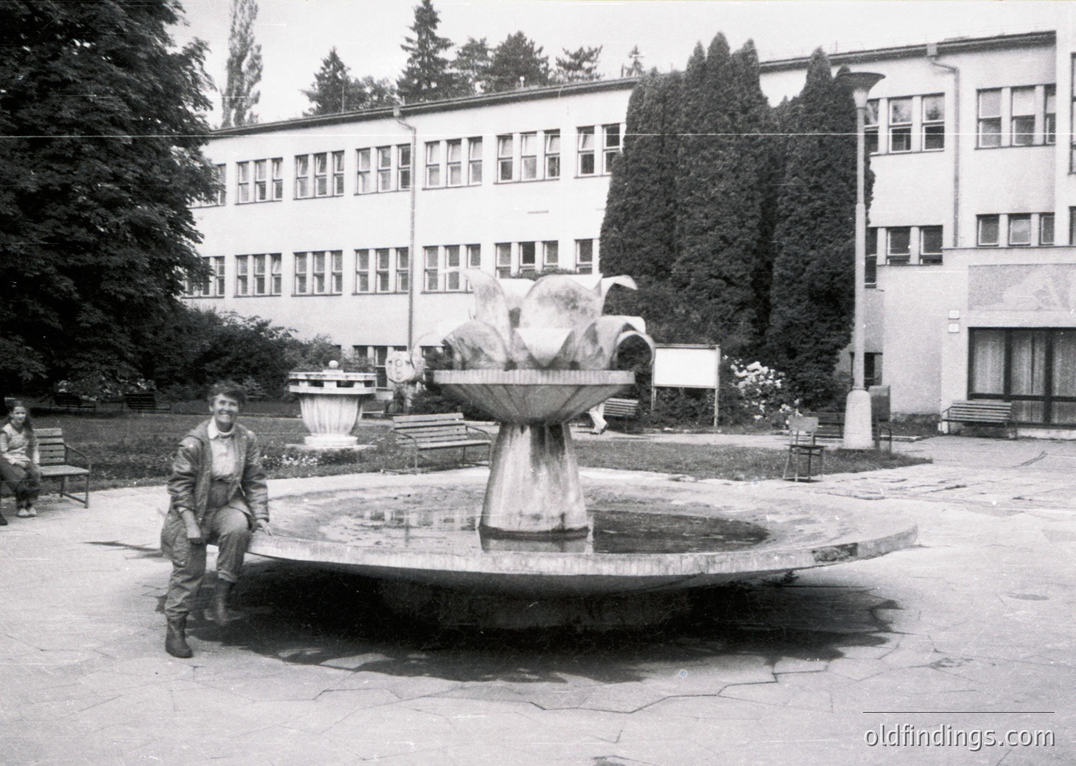 Mid-20th century courtyard with Soviet-era institutional building featuring symmetrical windows and concrete design. Central fountain with sculpted horse and rider. Man in military uniform poses near fountain, likely 1960s-1970s.