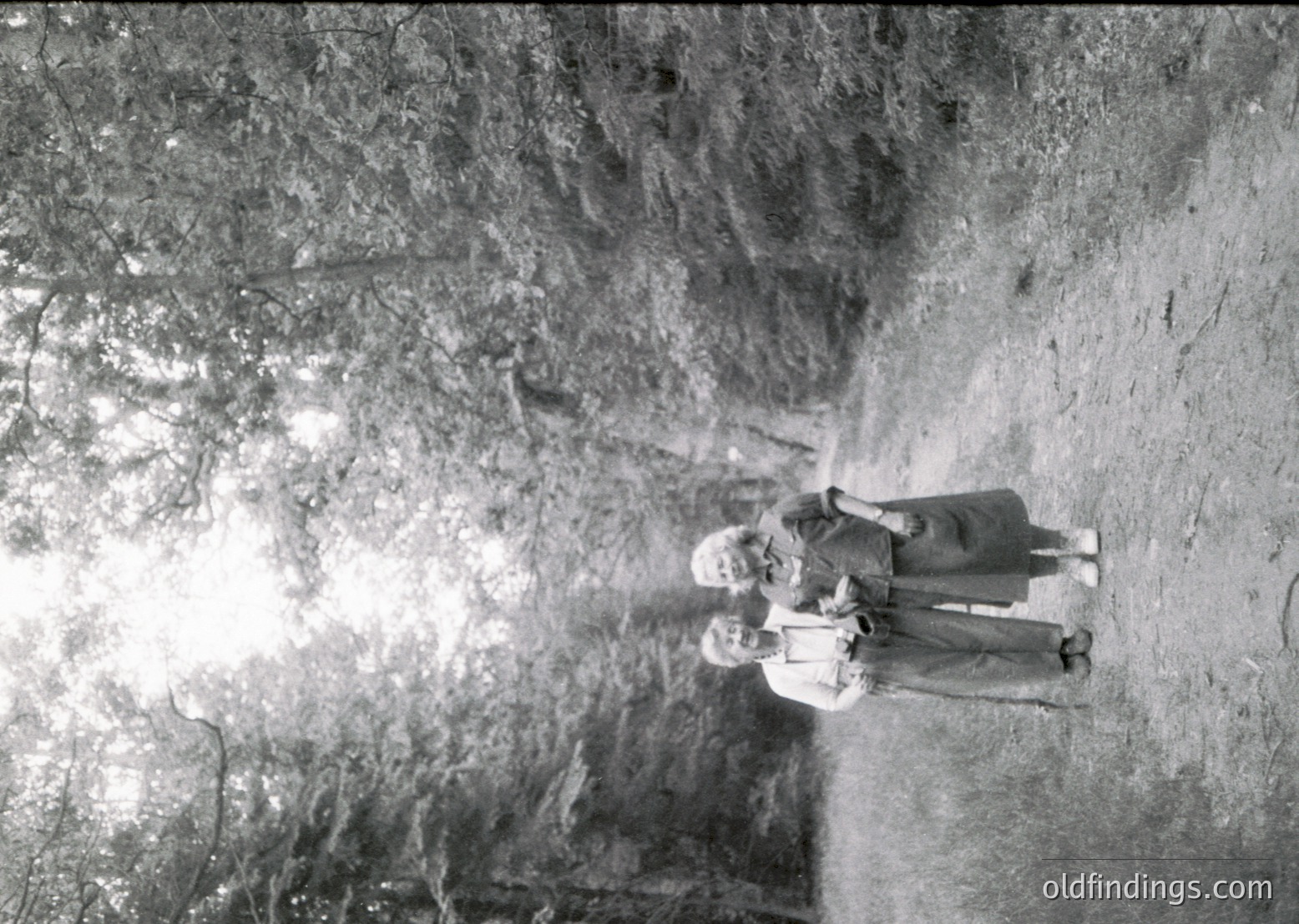 Two figures stand in a cavernous, sunlit rock formation, silhouetted against bright light. The vertical rock walls and natural lighting suggest an archaeological or geological site. Mid-20th century attire hints at mid-century exploration. Potential research value for geology, archaeology, or historical documentation.
