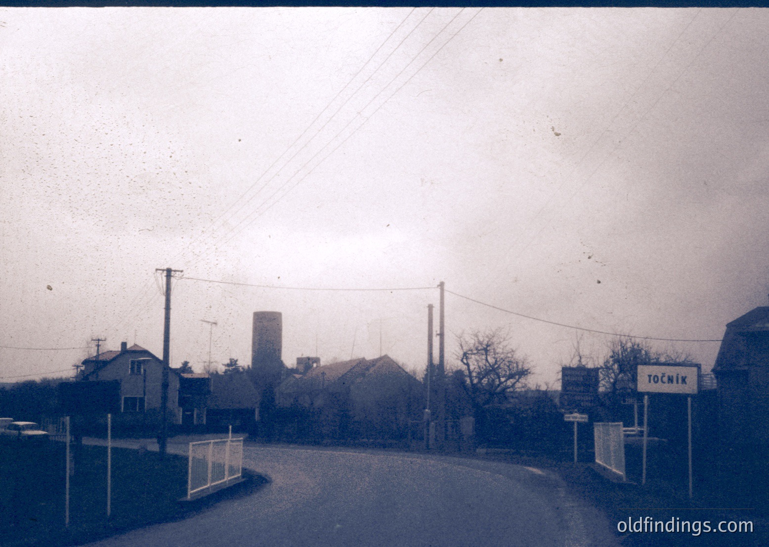 Vintage black-and-white street scene featuring a small industrial area with a tall brick chimney and residential houses. A signpost labeled "Точник" (Bulgarian for "Source") marks a road junction. Bare trees and utility poles suggest late autumn/winter. Likely Eastern European, 1950s–1970s.